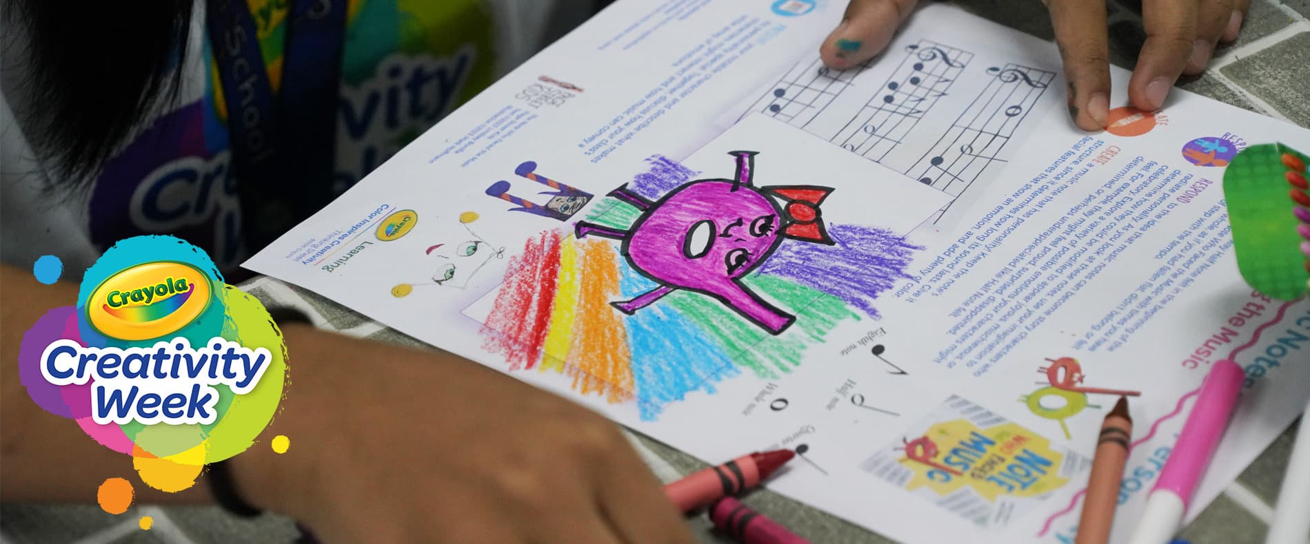 A child colouring a Crayola Creativity Week activity sheet with crayons